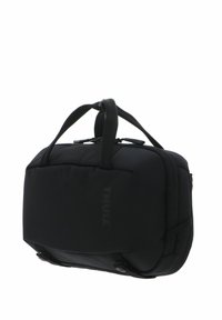 Sac souple compact Thule noir avec doubles poignées de transport et compartiments zippés, conçu pour les voyages ou l'usage quotidien.