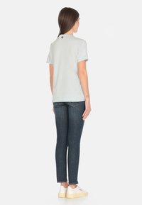 T-shirt di cotone azzurro chiaro con maniche corte, presenta un piccolo dettaglio sulla schiena. Abbinata a jeans blu scuro e sneaker bianche con suola color crema.