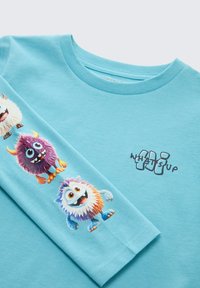 Blauwe lange mouw shirt met kleurrijke monsterafbeeldingen op de mouw en de tekst "What's Up" op de borst in een speelse lettertype.