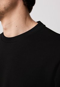 Zwarte t-shirt met een ronde halslijn en gladde stof. Close-up weergave die de textuur en pasvorm rondom het halsgebied benadrukt.