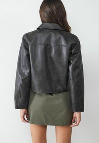 Giubbotto cropped in pelle nera con colletto a punta e dettagli di cucitura minimali, abbinato a una minigonna a righe verdi.