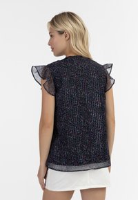 Top corto nero a fiori con maniche trasparenti arricciate; presenta righe verticali e un orlo posteriore leggermente più lungo.