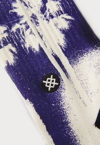 Κάλτσες φτιαγμένες από μαλακό ύφασμα, με γραφικό σχέδιο φοίνικα σε μωβ και λευκό χρώμα. Περιλαμβάνει λεπτομέρεια με μαύρο κεντημένο λογότυπο.