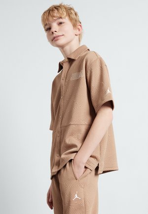 Light brown short-sleeve shirt with a textured geometric pattern and a button front. Features the "JORDAN" logo and a small logo on the sleeve.