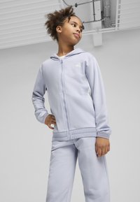 Gaiši purpursarkans zip-up džemperis ar balto logo, saskaņots ar atbilstošām sporta biksēm. Gluda tekstūra un ribināti stieptāji un josta.