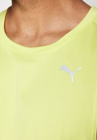 Puma spordipoolt särk erksas kollases värvuses, tekstuurse pinnaga ja hõbedase logoga vasakul rinnal. Ümar kaelus, lühikesed varrukad.