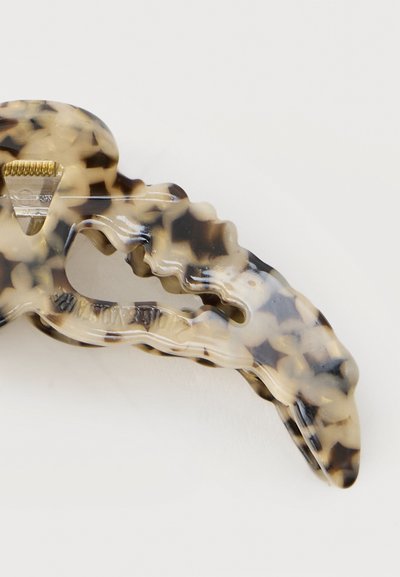 Pince à cheveux en plastique beige et noir à motif écailles de tortue avec mécanisme à ressort doré sur fond blanc.