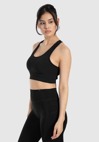 Sujetador deportivo negro, ajustado, con tirantes anchos, textura suave y detalles de costura. Combinado con leggings negros de cintura alta, ambos diseñados para ropa activa.