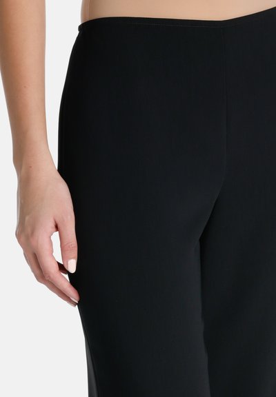Black stretch pants with a smooth texture and fitted design, held by a hand near the hip, showcasing the fabric's elasticity and shape.