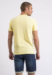 T-shirt à manches courtes jaune en tissu léger, associé à un short en denim foncé avec des revers et des poches arrière.