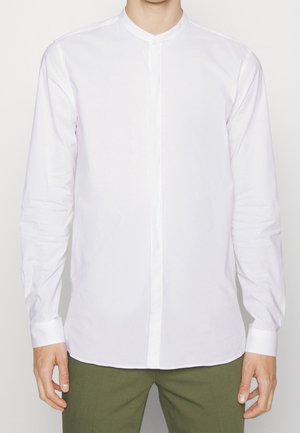 Witte longsleeve shirt met een bandkraag, gestructureerde pasvorm, zachte textuur, voorkant met verborgen knopen, gecombineerd met olijfgroene broeken.