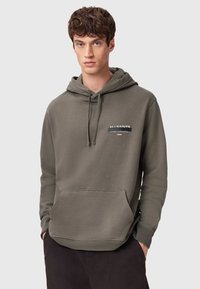 Oliwkowa zielona bluza z kapturem wykonana z miękkiego materiału, z przednią kieszenią, regulowanym sznurkiem przy kapturze oraz białym napisem na piersi.