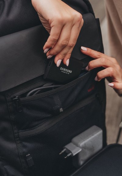 Zaino nero con una tasca in rete che mostra un SSD portatile Samsung e un caricatore, evidenziando il suo tessuto resistente e il design ordinato.