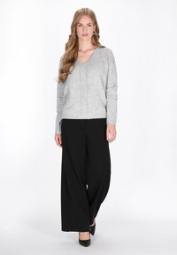 Grijze gebreide trui met een V-hals, gecombineerd met hoge zwarte wijde broek en zwarte puntige hakken.