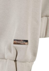 Light beige sweatshirt fabric with ribbed texture and gathered detailing. Features a silver rectangular tag with "Dropside" engraved.