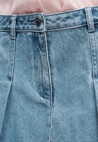 Τα ανοιχτόγαλαζα τζιν σορτς διαθέτουν ψηλή μέση με κούμπωμα σε κουμπί, εμπρόσθιες τσέπες και εμφανείς ραφές. Η υφή του υφάσματος είναι απαλή.