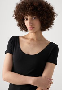 Svart kortärmad topp med rundad halsringning, tillverkad av ett mjukt och slätt tyg. Har en figurnära design som framhäver en ren och minimalistisk look.