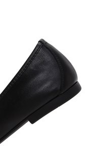 Ballerine en cuir noir avec un bout arrondi et une semelle noire basse. La surface est lisse avec des détails de couture subtils.