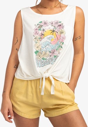 Biała bezrękawnikowa bluzka z kwiatowym wzorem graficznym i wiązaniem w talii, zestawiona z żółtymi, wysokim stanem szortami.