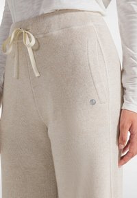 Lichtbeige joggingsbroek van textuurstof, met een trekkoord in de taille, zijzakken en een klein logodetail.