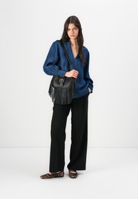 Mörkblå denimskjorta i lös passform med långa ärmar; svart crossbody-väska med fransar; svarta vida byxor; djurprintade ballerina-skor.
