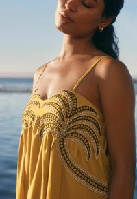 Robe sans manches jaune avec broderie de feuilles de palmier en blanc et noir, présentant une coupe ample et un tissu doux pour le confort.
