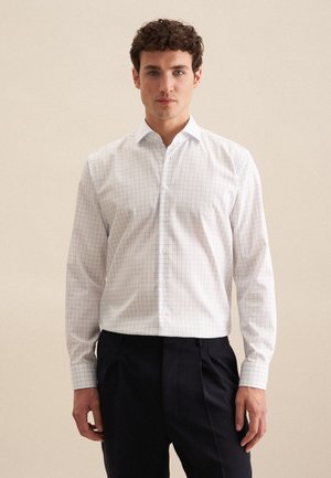 Chemise blanche à manches longues avec un motif à carreaux bleus, col boutonné et tissu léger, associée à un pantalon sombre.