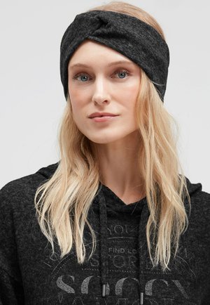 Black knit headband featuring a twisted front design with a soft texture. Worn with a dark hooded sweatshirt.