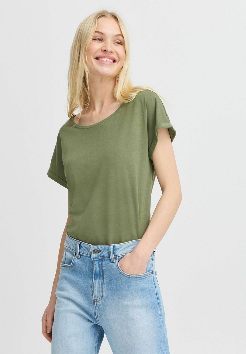 Camiseta de manga corta verde oliva con un corte relajado, escote redondo, combinada con unos pantalones vaqueros de tiro alto color azul claro. Textura de tela suave y lisa.