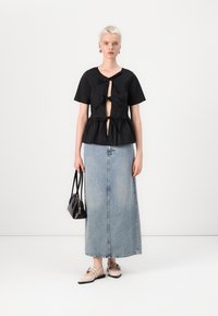 Svart peplumtopp med korte ermer og detalj med knytte foran. Kombinert med et lys blått denim maxiskjørt. Tilbehøret inkluderer en liten svart håndveske.