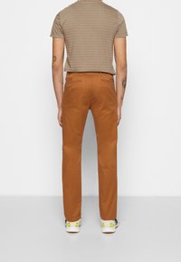 Brązowe bawełniane spodnie o prostym kroju, zestawione z szarą, paskowaną koszulką. Stylizacja uzupełniona białymi i żółtymi sneakersami.