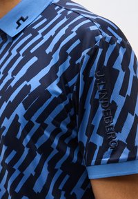 Μπλε και ναυτικό μπλουζάκι πόλο με αφηρημένο σχέδιο βούρτσας και το κέντημα "J.LINDEBERG" στο μανίκι.