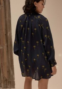 Marineblauwe lange jurk met gouden bloemenborduursels. Losse pasvorm, geplooide achterkant en manchetten. Transparante stof met een zachte textuur.