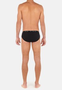 Schwarze Baumwollunterhosen mit einem schwarzen Bund, der das weiße "HOM"-Logo trägt, enganliegendes Design, das eine glatte Textur und minimale Bedeckung zeigt.