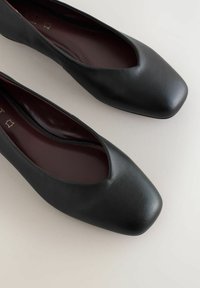 Musta nahkainen ballerinatyyppinen kengät, joissa on neliön muotoinen varvas ja sileä pinta. Sisäpuolella on tumman viininpunainen vuori ja matala profiilimuotoilu.