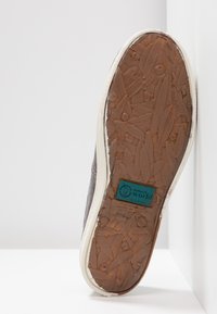 Sola di sneaker grigia con un motivo in gomma marrone testurizzato. Presenta un bordo bianco e un'etichetta turchese che indica materiali ecologici.