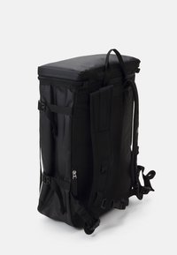 Czarny plecak o wyraźnym prostokątnym kształcie, z zapięciem na zamek u góry, regulowanymi paskami oraz bocznymi klamrami. Wykonany z trwałego, teksturowanego materiału.