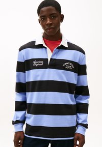 Polo a manica lunga con righe nere e azzurre, colletto bianco. Loghi frontali con le scritte "American Originals" e "TOMMY JEANS".