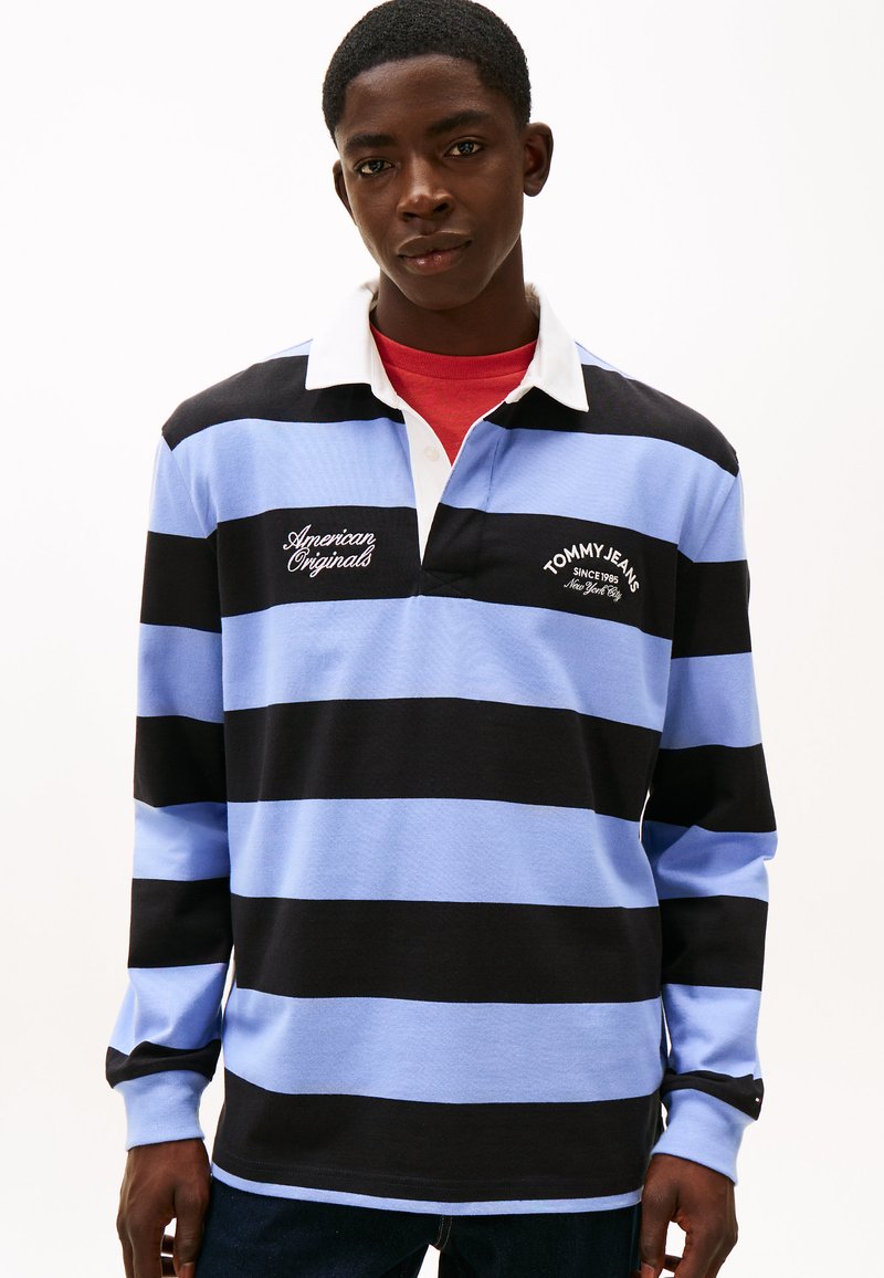 Polo a manica lunga con righe nere e azzurre, colletto bianco. Loghi frontali con le scritte "American Originals" e "TOMMY JEANS".