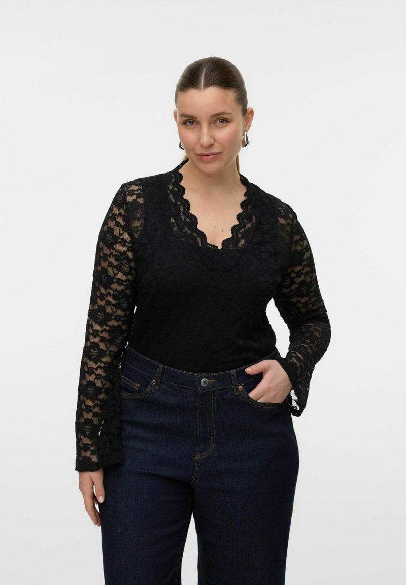 Haut à manches longues en dentelle noire avec un col en scallops et un motif floral complexe, associé à un jean en denim foncé avec des poches avant.