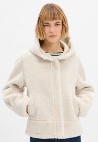 Crèmekleurige fleec jacket met een capuchon, voorzien van een volledige ritssluiting aan de voorkant, grote zakken en een gestructureerd, zacht oppervlak.