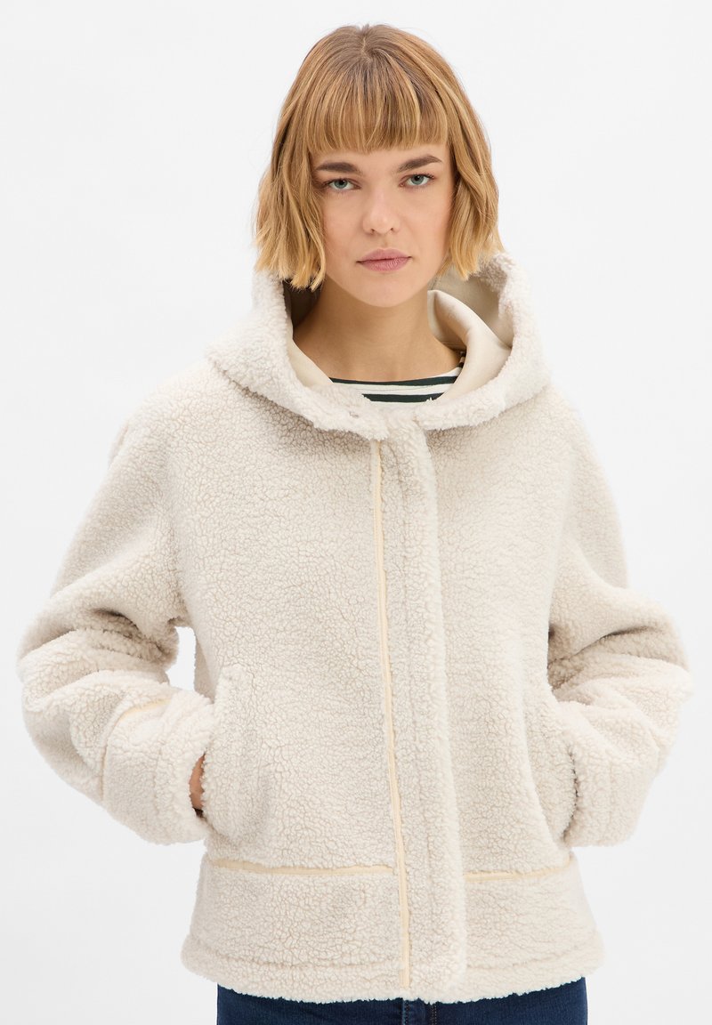 Crèmekleurige fleec jacket met een capuchon, voorzien van een volledige ritssluiting aan de voorkant, grote zakken en een gestructureerd, zacht oppervlak.