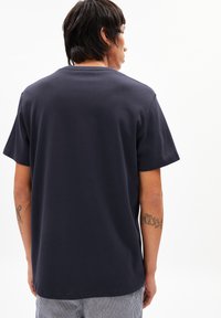 T-shirt en coton bleu marine avec un col rond et des manches courtes, présentant un dos uni et une coupe décontractée. Design minimaliste sans logos visibles.