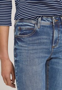 Jeans de mezclilla azul con un diseño ajustado, que presentan un estilo clásico de cinco bolsillos, un botón de latón y un ligero desgaste a lo largo de las piernas.