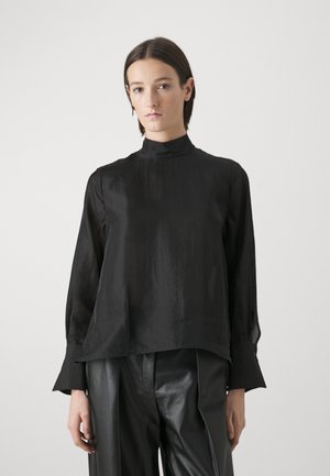 Czarny longsleeve z gładkiego materiału z wysokim kołnierzem, o luźnym kroju i szerokimi mankietami, zestawiony z czarnymi spodniami wysokim stanie.