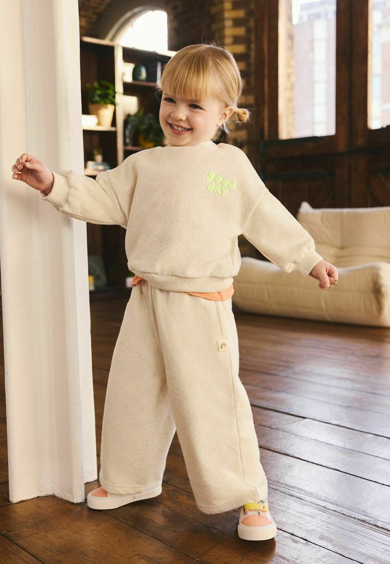 Suéter color crema con texto verde "buen día", combinado con pantalones de pierna ancha a juego y zapatillas pastel. Tela suave y texturizada.