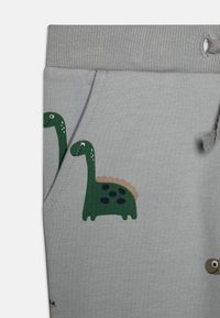 Pantaloni della tuta grigi in cotone con stampe di dinosauri verdi, caratterizzati da una texture morbida, un elastico in vita e dettagli con tasche laterali.