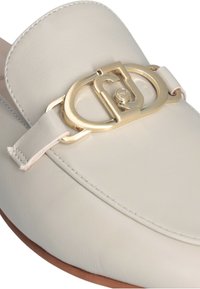 Scarpa slip-on in pelle bianca con un'importante fibbia in metallo dorato e una superficie liscia, punta arrotondata e bordi morbidi.