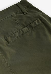 Pantaloni verde măsliniu cu un buzunar posterior cu clapetă cusută, textură netedă și cusături îngrijite. Un detaliu de design versatil și casual.