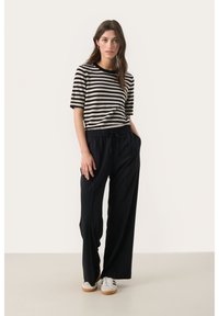 T-shirt rayé noir et crème à manches courtes, associé à un pantalon de survêtement noir ample avec une taille élastique et des poches latérales.
